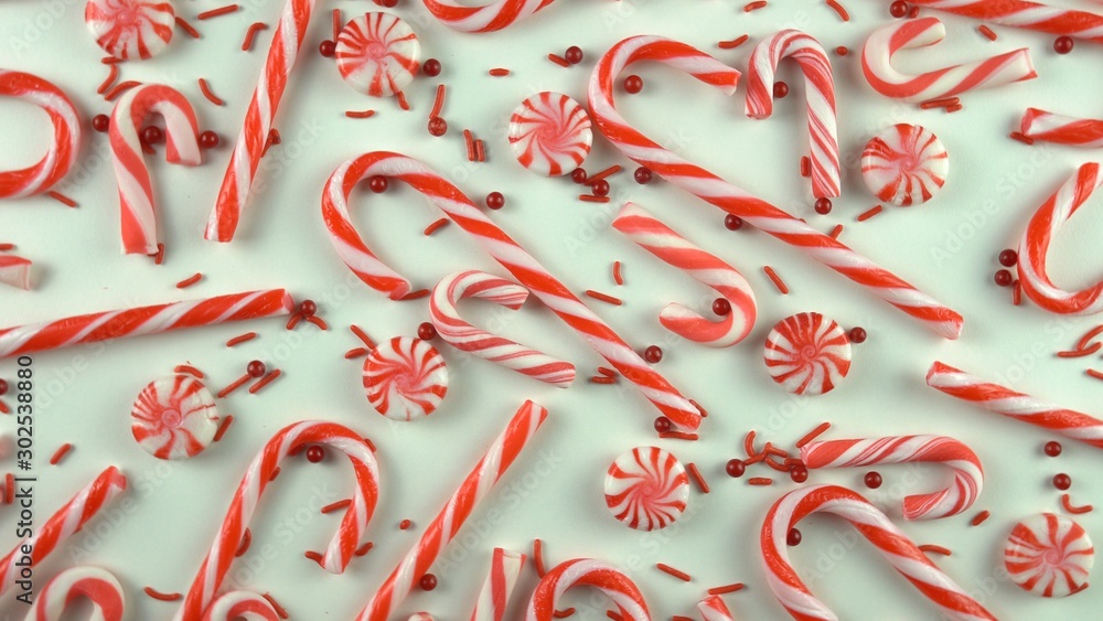 Close up of Christmas Eve season red color mood table with candy canes and peppermint spinning over white background. Holiday scene with pearls sprinkles. Close up of Christmas Eve season red color mood table with candy canes and peppermint spinning over white background. Holiday scene with pearls sprinkles.