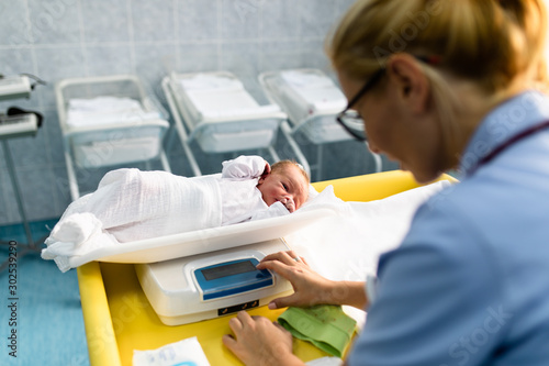 Young nurse working in maternity ward. She measuring weight and wrapping the newborn baby. photo