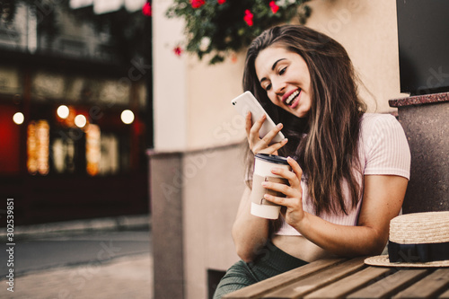 Beautiful woman using phone and drink coffee sitting on street cafe.