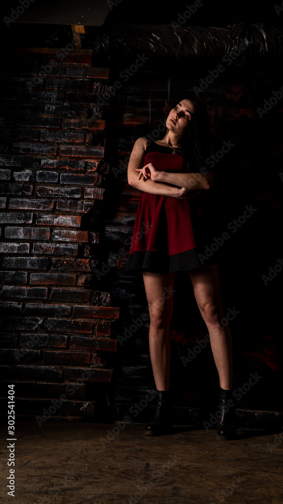 Pretty young sexy model female with dark hair in amazing long red dress and black shoes posing in dark studio Pretty young sexy model female with dark hair in amazing long red dress and black shoes posing in dark studio