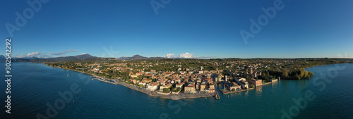 Aerial view of Lake Garda and the historic city center of Lazise, Italy. Autumn and winter season, clear blue sky, Alps on the horizon, snow in the mountains