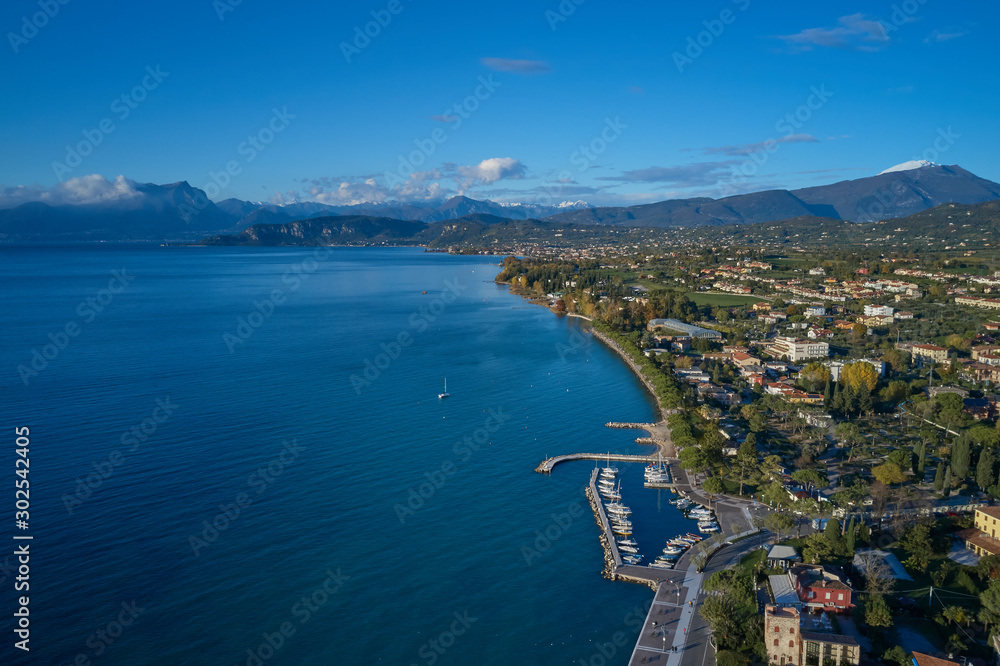 Aerial view of Lake Garda and the boat parking of Lazise, Italy. Autumn season, blue sky, Alps on the horizon, snow in the mountains