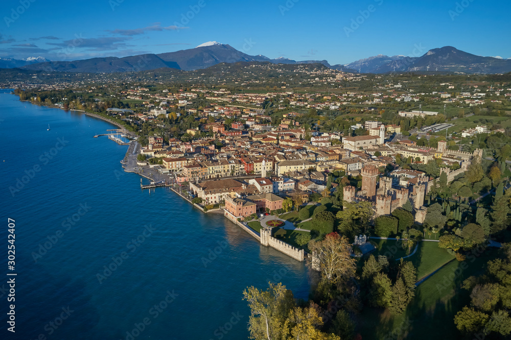 Aerial view of Lake Garda and the city center of Lazise, Italy. Autumn season, blue sky, Alps on the horizon, snow in the mountains