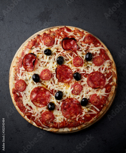 Pizza with chorizo, mozzarella cheese, cherry tomatoes, black olives and oregano. Home made food. Concept for a tasty and hearty meal. Black stone background. Top view. 