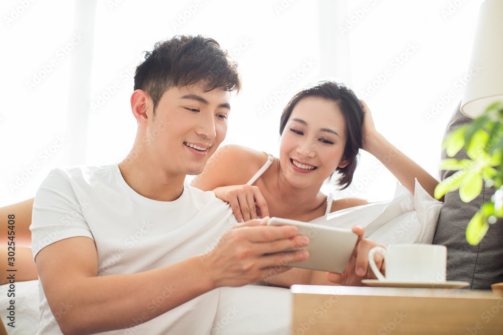 Happy young Chinese couple using smartphone in bedroom Happy young Chinese couple using smartphone in bedroom