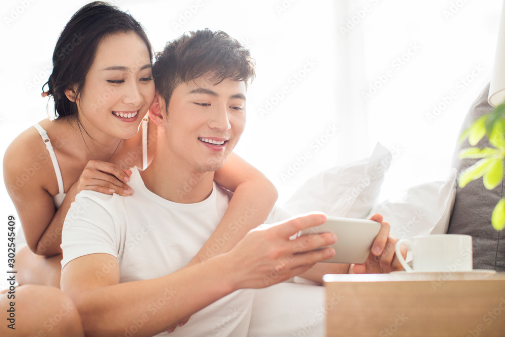 Happy young Chinese couple using smartphone in bedroom Happy young Chinese couple using smartphone in bedroom