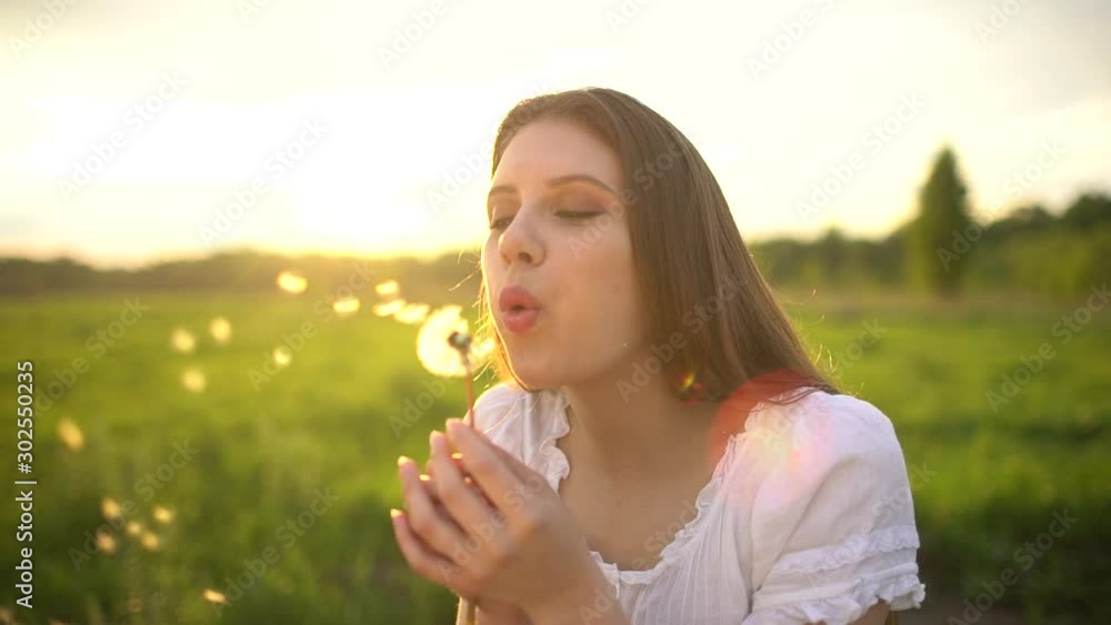 Smiling beautiful woman hugging enjoying nature summer at sun day. having fun outdoors. Caucasian happy teenage girl blowing dandelions in summer countryside at sunset, slow-motion