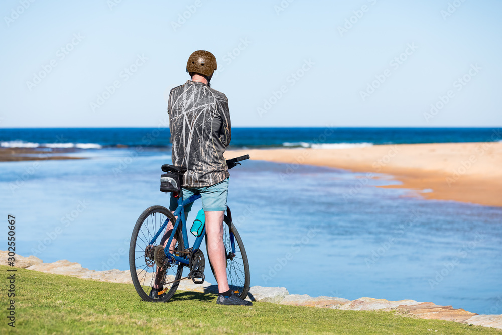 Fototapeta premium An unidentifiable man on a blue bicycle sits by the sea at the beach on a sunny day. Copy space.