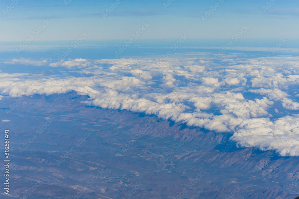 clusters of white clouds visible from above in the sky and mountains clusters of white clouds visible from above in the sky and mountains