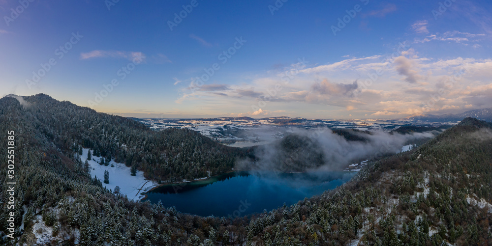 lake alatsee in bavaria at winter with sunset view to forest and  fuessen