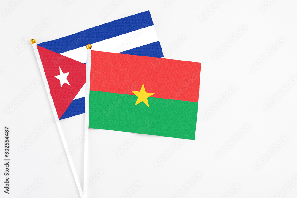Naklejka premium Burkina Faso and Cuba stick flags on white background. High quality fabric, miniature national flag. Peaceful global concept.White floor for copy space.