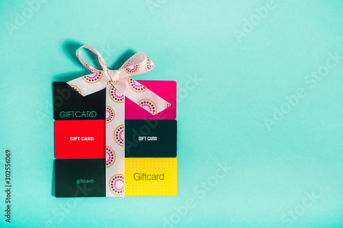 Top view colourful Shop gift cards in shape of present box with a bow of satin ribbon on bright turquoise background. Creative ideas for presents. Flat lay. Holiday sales mockup with copy space. photo