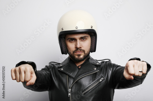 Portrait of young biker in a leather jacket pretending to ride a motorcycle isolated on a white background. Horizontal. © face_reader_img