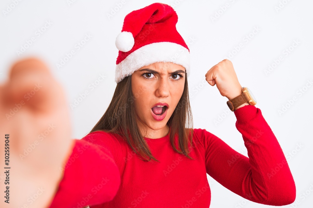 Girl wearing Christmas Santa hat make selfie by camera over isolated white background annoyed and frustrated shouting with anger, crazy and yelling with raised hand, anger concept Girl wearing Christmas Santa hat make selfie by camera over isolated white background annoyed and frustrated shouting with anger, crazy and yelling with raised hand, anger concept