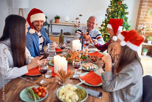 Beautiful family wearing santa claus hat meeting smiling happy and confident. Eating roasted turkey using smartphone celebrating Christmas at home