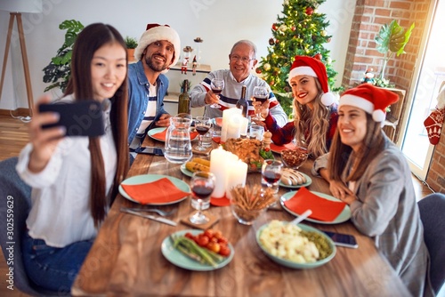 Beautiful family wearing santa claus hat meeting smiling happy and confident. Eating roasted turkey make selfie by smartphone celebrating Christmas at home © Krakenimages.com