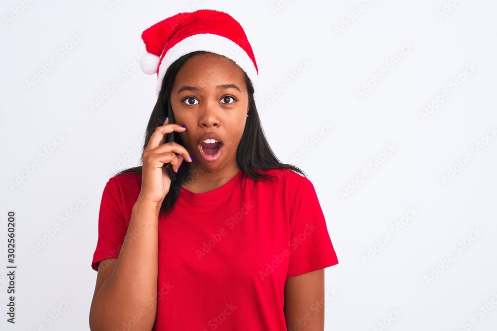 Young african american woman wearing christmas hat and talking on smartphone scared in shock with a surprise face, afraid and excited with fear expression Young african american woman wearing christmas hat and talking on smartphone scared in shock with a surprise face, afraid and excited with fear expression