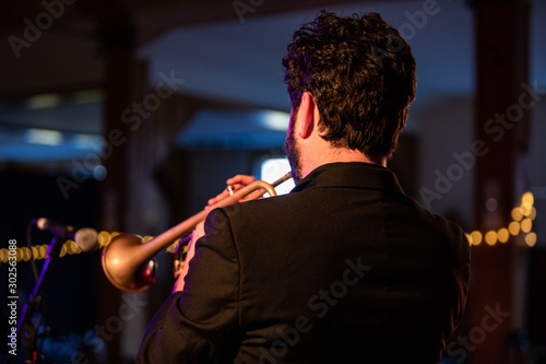 Backside view of an adult man playing music on his wind instrument on stage while giving a live performance 