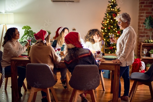 Beautiful group of women smiling happy and confident. On of them holding cup of wine speaking speech celebrating christmas at home