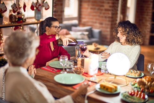 Beautiful group of women smiling happy and confident. Eating roasted turkey and serving wine on cup celebrating christmas at home