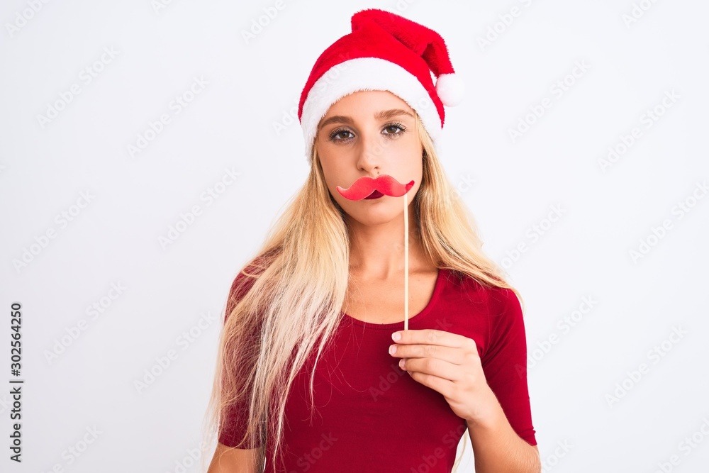 Woman wearing Christmas Santa hat holding fanny mustache over isolated white background with a confident expression on smart face thinking serious Woman wearing Christmas Santa hat holding fanny mustache over isolated white background with a confident expression on smart face thinking serious