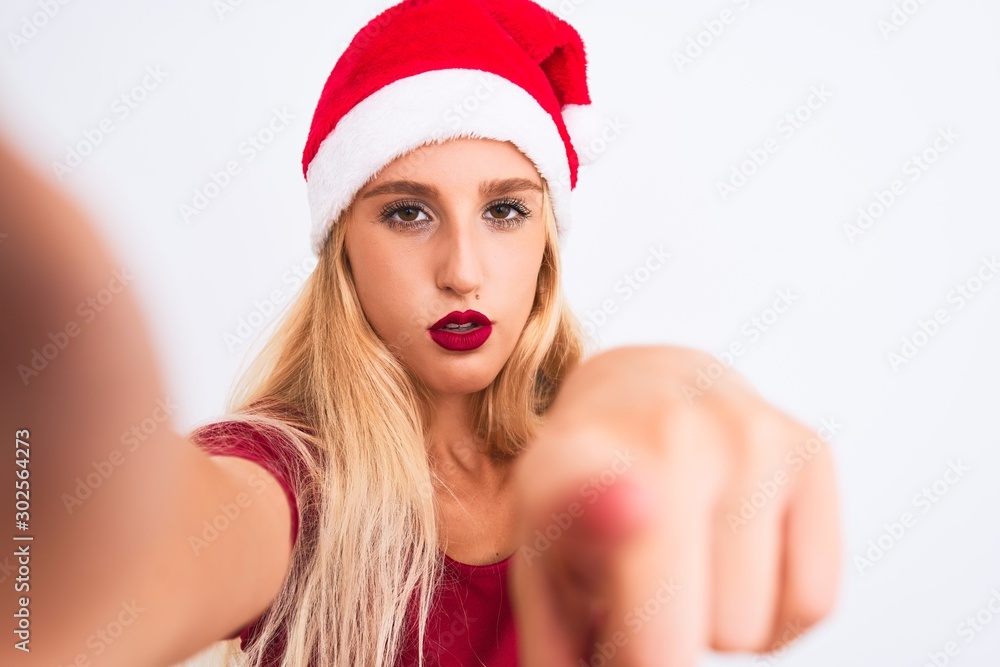 Woman wearing Christmas Santa hat make selfie by camera over isolated white background pointing with finger to the camera and to you, hand sign, positive and confident gesture from the front Woman wearing Christmas Santa hat make selfie by camera over isolated white background pointing with finger to the camera and to you, hand sign, positive and confident gesture from the front