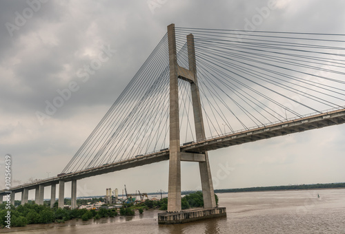 Ho Chi Minh City, Vietnam - March 12, 2019: Long Tau and song Sai Gon rivers meeting point. Landscape with H-shaped pylon of Phu My suspension bridge in center under gray cloudscape. Brown water.