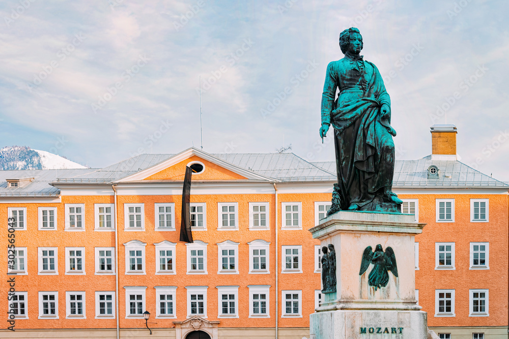Fototapeta premium Mozart monument on Mozartplatz Square in Old city of Salzburg of Austria, Europe at winter. Wolfgang Amadeus Statue on street. View on Sculpture in Austrian town of Salzburgerland. Sky with clouds.