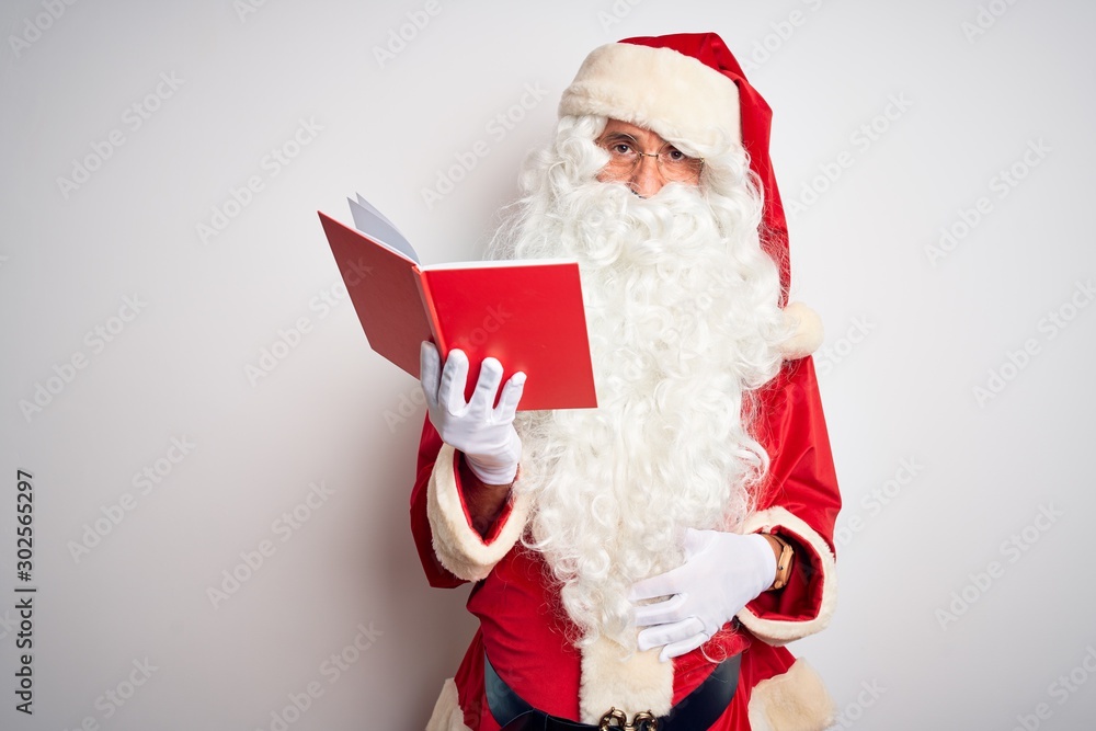Naklejka premium Middle age man wearing Santa Claus costume reading book over isolated white background Relaxed with serious expression on face. Simple and natural looking at the camera.