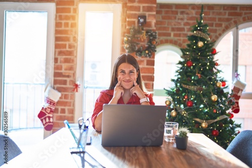 Beautiful woman sitting at the table working with laptop at home around christmas tree Smiling with open mouth, fingers pointing and forcing cheerful smile