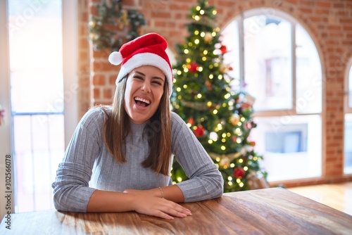 Young beautiful woman wearing santa claus hat at the table at home around christmas decoration with a happy and cool smile on face. Lucky person.