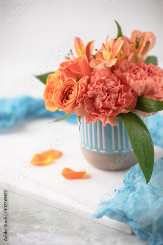 Floral arrangment of orange roses, carnations, and alstroemeria in teal vase on white background.