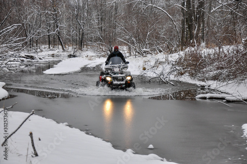 An ATV on wheels crosses a frozen river breaking ice
