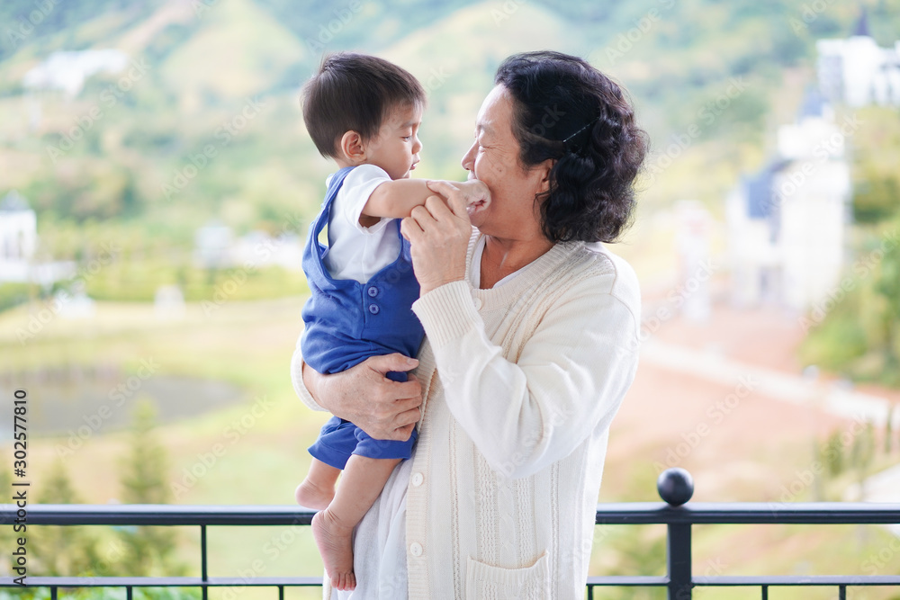 Happy and healthy asian grandmother is holding and playing with grandchild in the morning time on the background of nature, concept of multi generation living of asian family lifestyle. Happy and healthy asian grandmother is holding and playing with grandchild in the morning time on the background of nature, concept of multi generation living of asian family lifestyle.