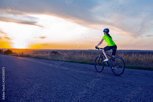 Beautiful sport girl cyclist riding a bike on the road towards the sunset. Nature and recreation. Hobbies and sports