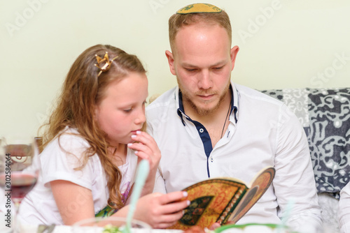 Jewish family celebrate Passover Seder reading the Haggadah. Selective focus on man. photo