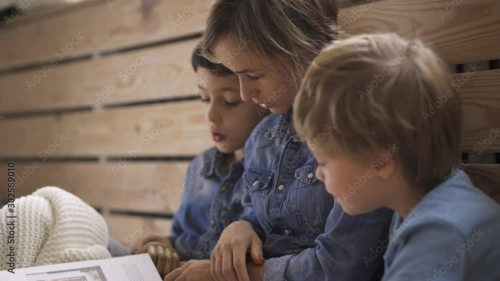 Young caucasian woman reads a book to two sons sitting on the floor. A beautiful young mother is reading a book. Young caucasian woman reads a book to two sons sitting on the floor. A beautiful young mother is reading a book.