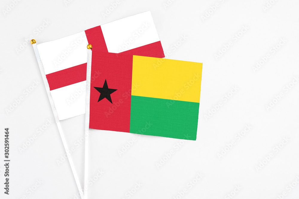 Guinea Bissau and England stick flags on white background. High quality fabric, miniature national flag. Peaceful global concept.White floor for copy space.