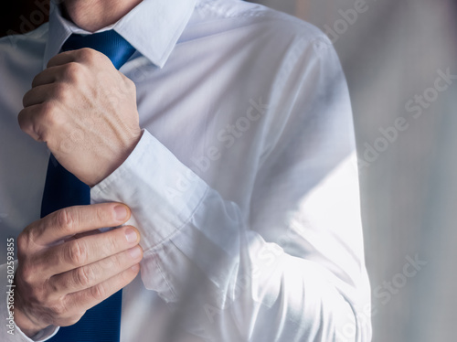 Businessman in a white shirt with a blue tie bowtie buttons a button on his hand.