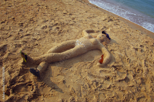 A man made of sand lies on the beach. Vacation concept. Sandman