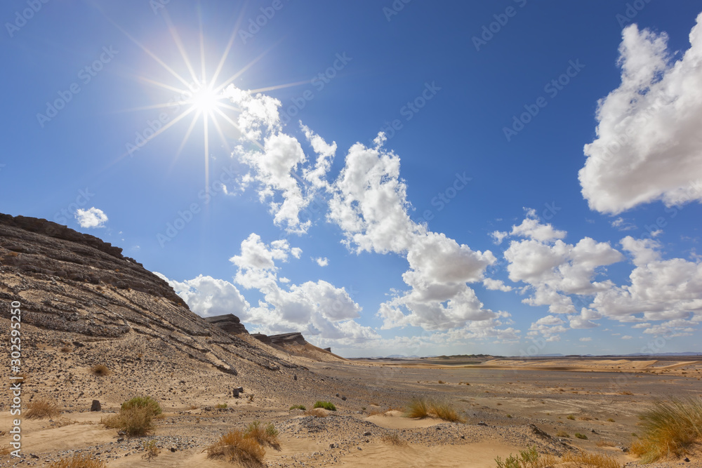 Fototapeta premium Desert landscape with cloudy blue sky and sun starburst.