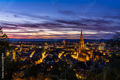Germany, Illuminated night lights of skyline freiburg im breisgau aerial view over cityscape, roofs, houses, streets and famous minster cathedral by night