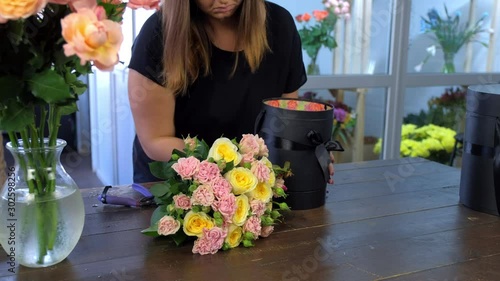 Professional florist woman making bouquet of roses putting it in packaging black box, closeup hands. Floral business concept. Creates bunch composition in floristic studio store.