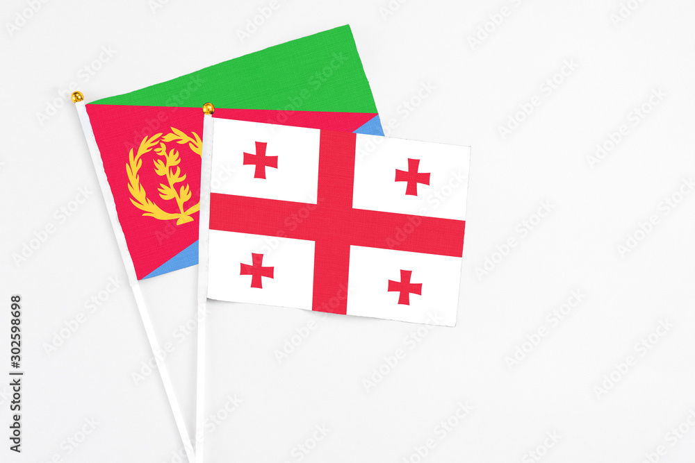 Georgia and Eritrea stick flags on white background. High quality fabric, miniature national flag. Peaceful global concept.White floor for copy space.