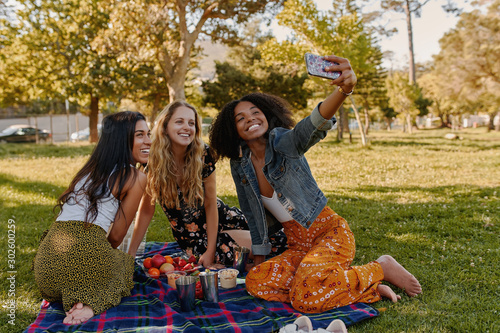 Obraz na plátně Group of happy diverse three female friends sitting together on blanket over the