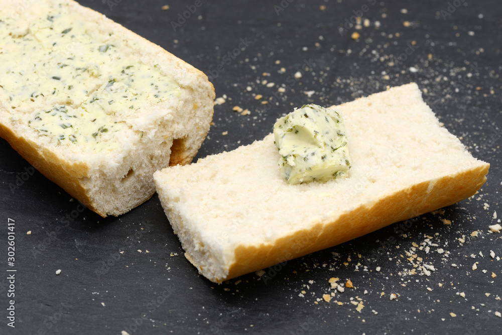 rustic crusty white bread with Herb butter lying on black slate in the kitchen