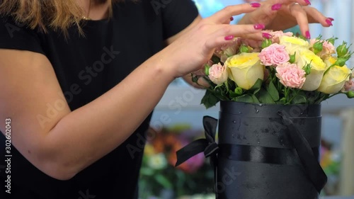 Professional florist woman making bouquet of roses in packaging black box, closeup hands. Floral business concept. Creates bunch composition in floristic studio store. Beautiful pink yellow flowers.