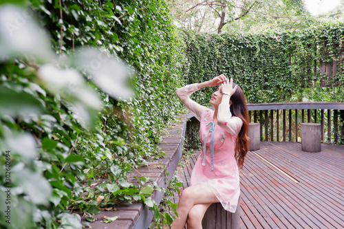 Young beautiful asian woman sitting in wooden chair with  plant wall photo