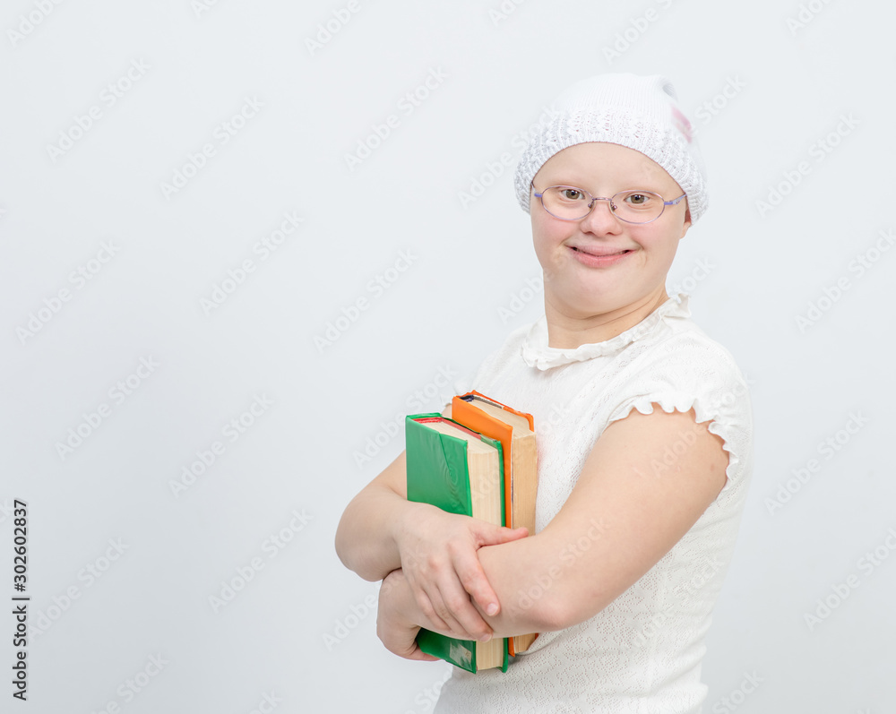 A girl with Down Syndrome stands with books on gray background. Empty space for text A girl with Down Syndrome stands with books on gray background. Empty space for text