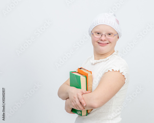 A girl with Down Syndrome stands with books on gray background. Empty space for text